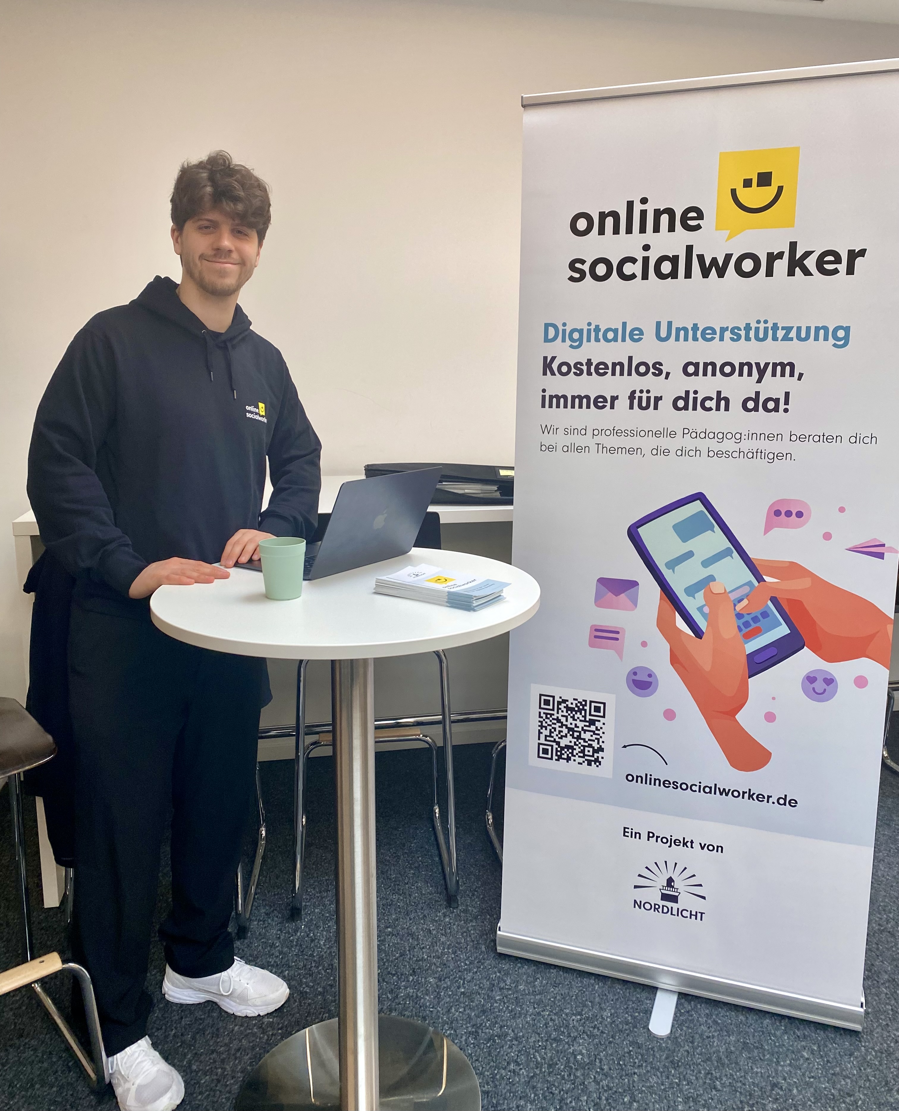 Ein Mann steht an einem Infostand zum Thema Online Socialworker