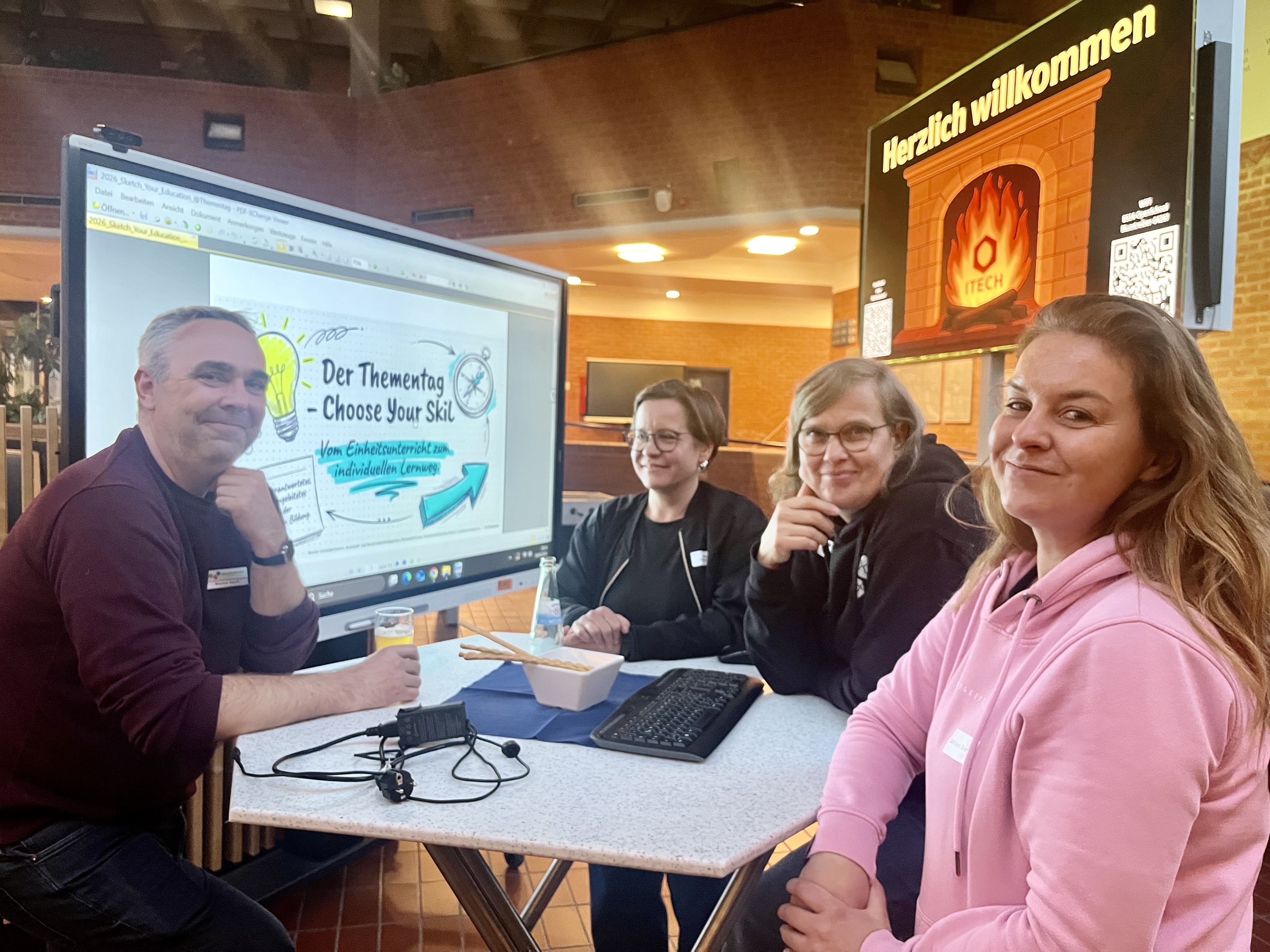 ZweiGäste und zwei Lehrkräfte stehen vor einem Smartboard udn tauschen sich über den Thementag aus.